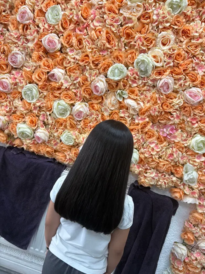 Glossy straight dark hair photographed against the salon flower wall